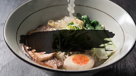 湯気の立つ豚骨ラーメン。チャーシュー、味玉、青菜、ねぎ。