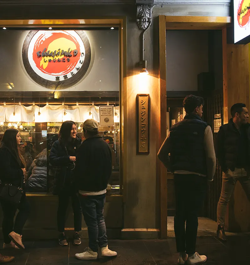 夜のラッセル通り本店。「シュジンコウ本店」の看板の前に並ぶ客。